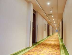 Ein langer, schmaler Hotelkorridor mit Türen an beiden Seiten, einem gemusterten Teppich und eingelassener Deckenbeleuchtung.