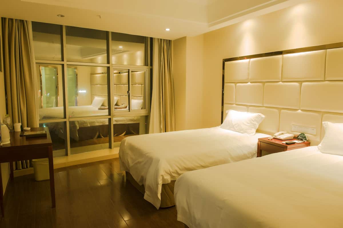 A hotel room with two beds, a desk, and a large window with curtains.