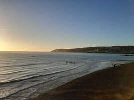 A beach with a clear sky, calm sea, and a distant hill with buildings.