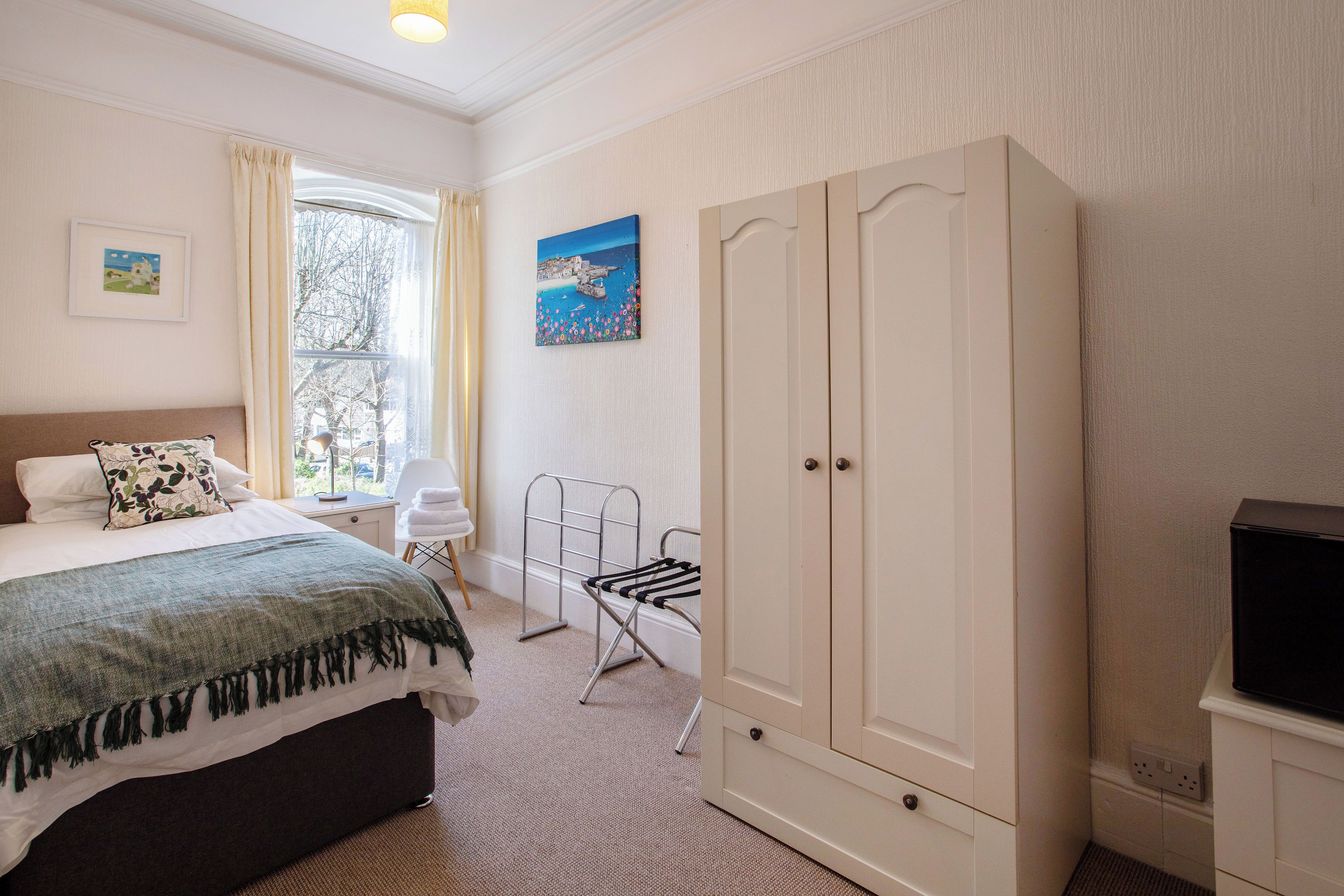 Ein Schlafzimmer mit einem Bett, einem Kleiderschrank, einem Fernseher, einem Fenster mit Vorhängen und einem Bild an der Wand.