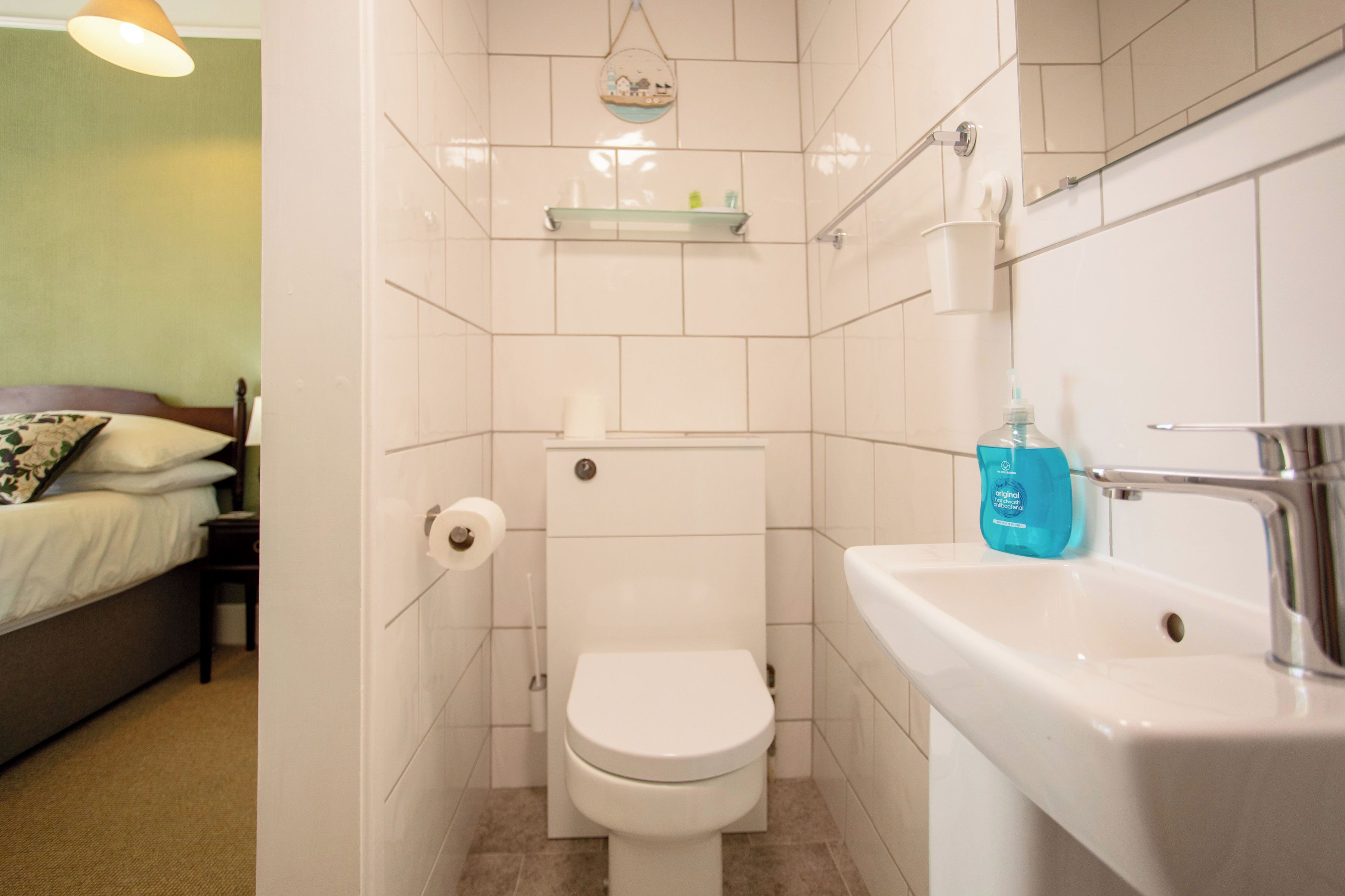 A small bathroom with a toilet, sink, and a shelf above the toilet.