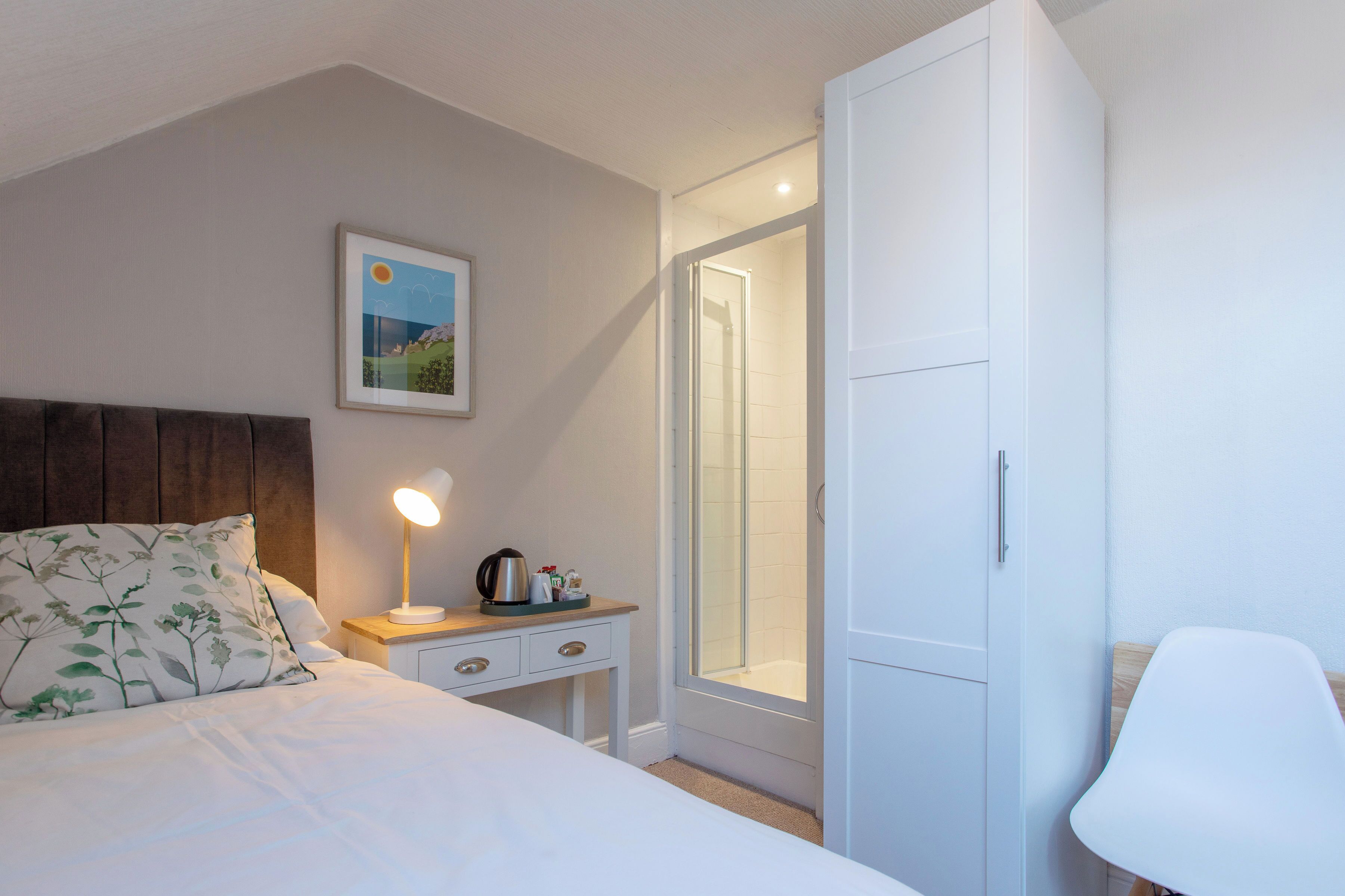 Ein Schlafzimmer mit Bett, Nachttisch mit Lampe, Schrank und einer Duschkabine.