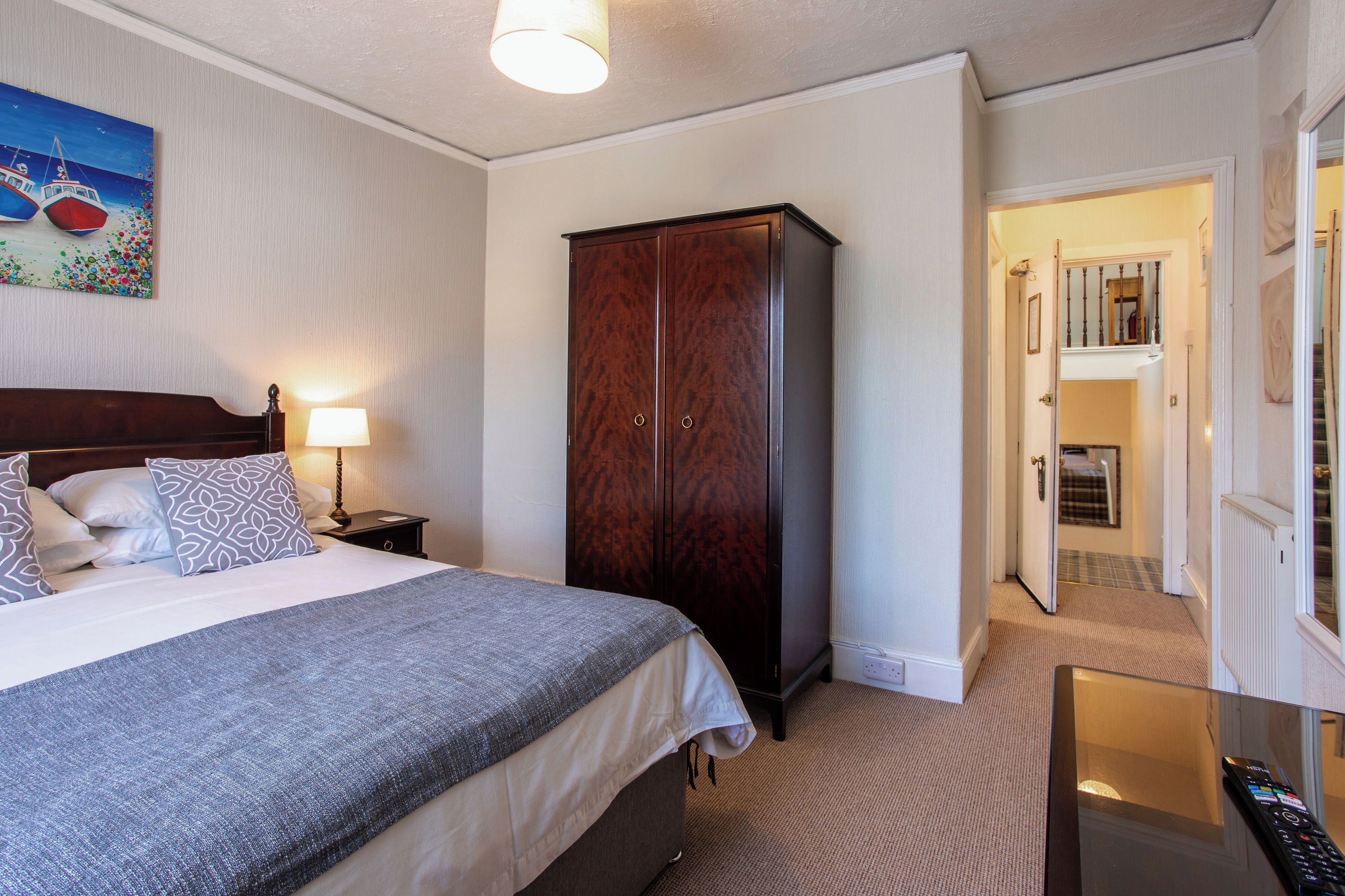 Una habitación de hotel con cama, armario, mesita de noche y un cuadro en la pared.