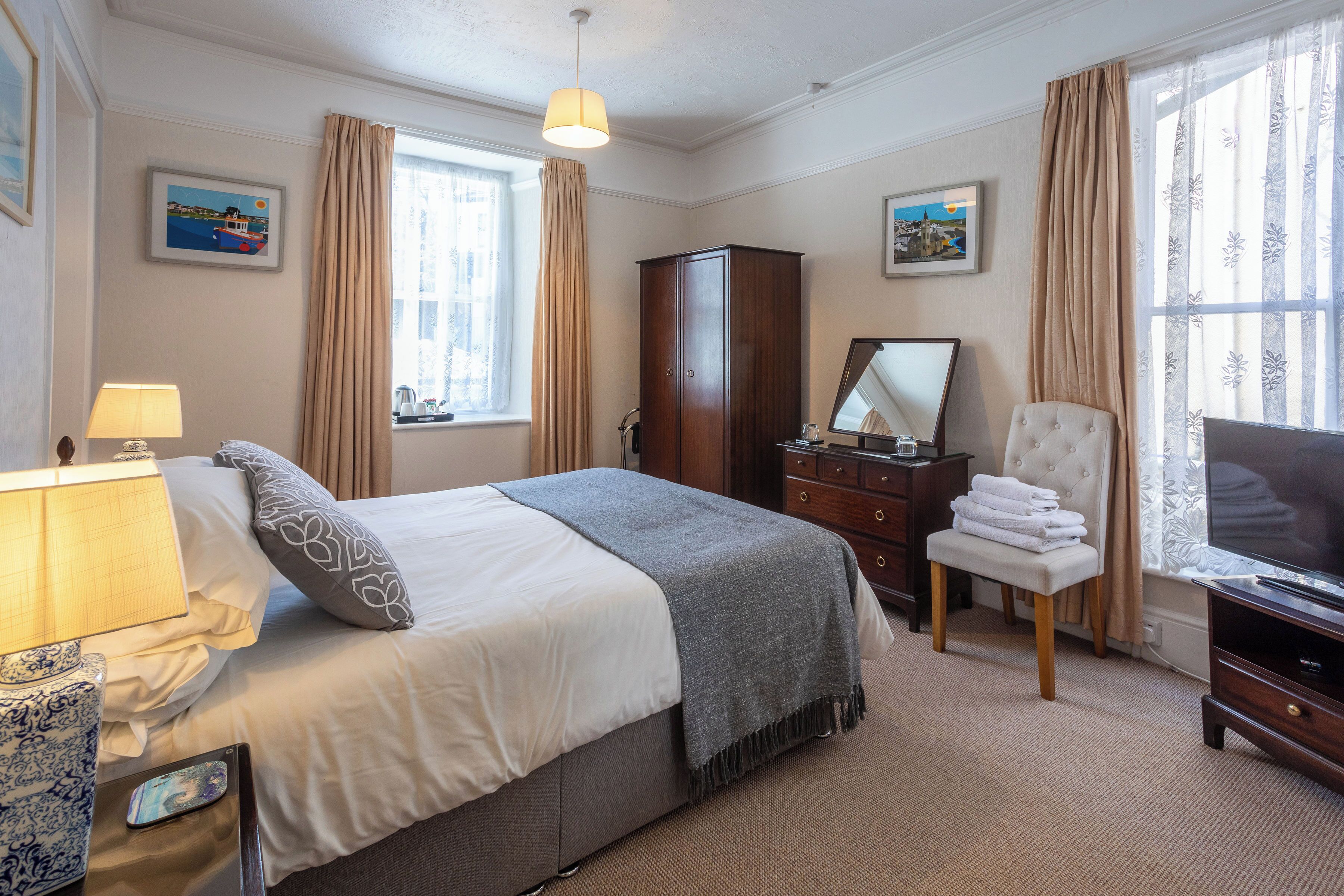 A neatly arranged hotel room with a bed, bedside table, lamp, wardrobe, chair, and a television.