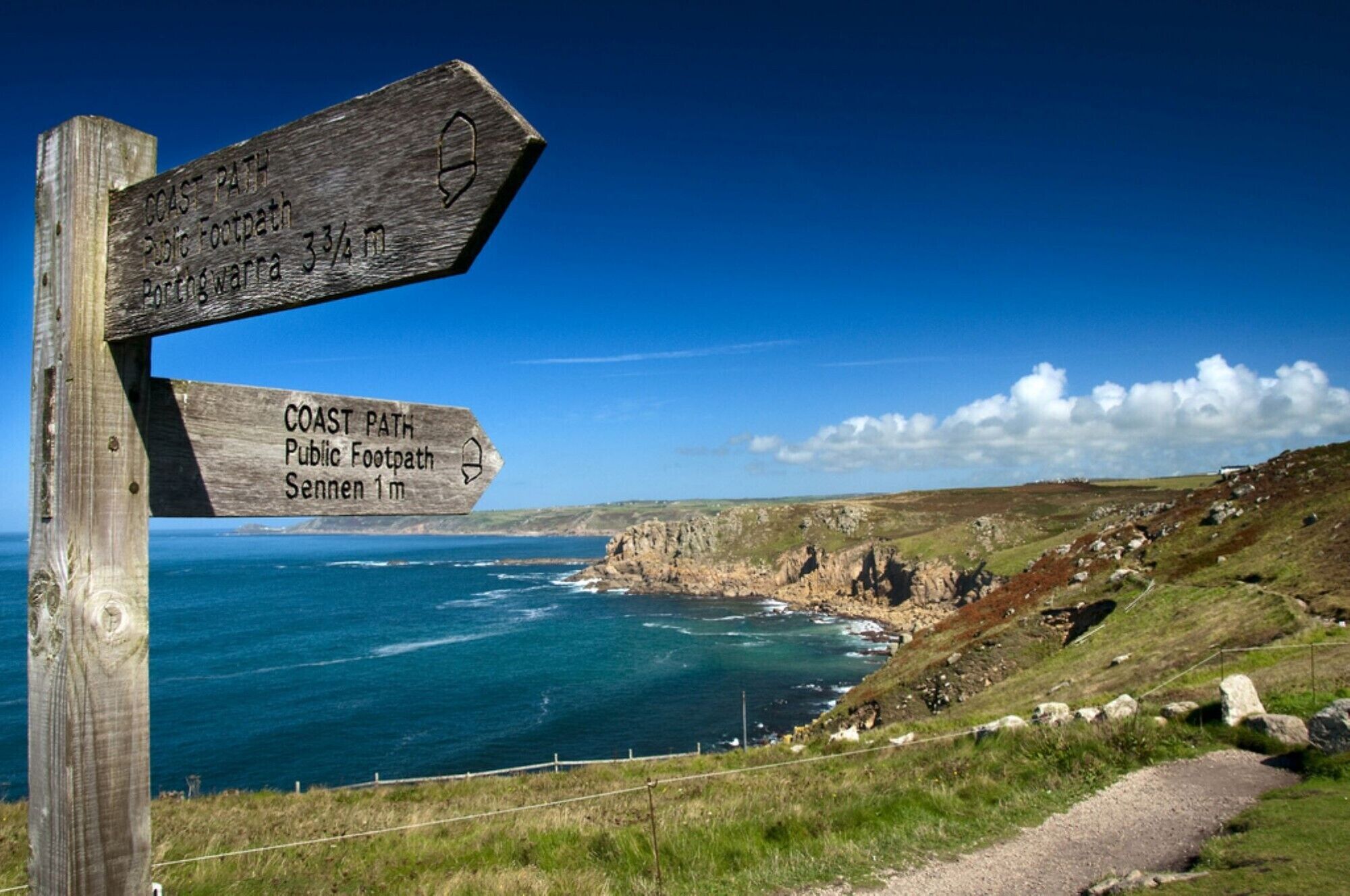 A wooden signpost with directions to 'Coast Path Public Footpath' and 'Portogarra 3½m'.