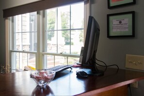 A desk with a computer, keyboard, and mouse, a bowl of candy, and a window with a view of the outdoors.