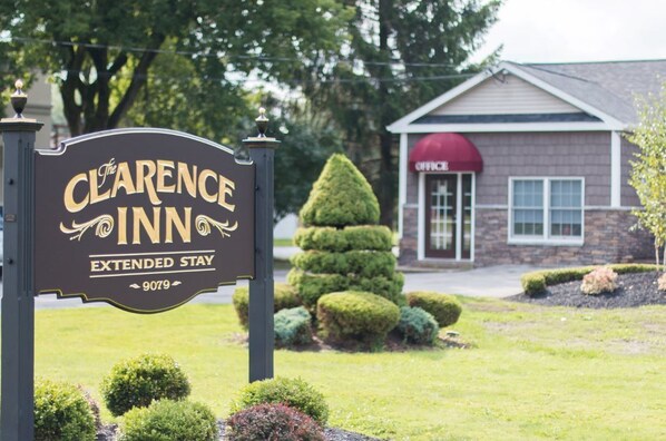 A sign for Clarence Inn Extended Stay, a brick building with a red awning, and well-maintained landscaping.
