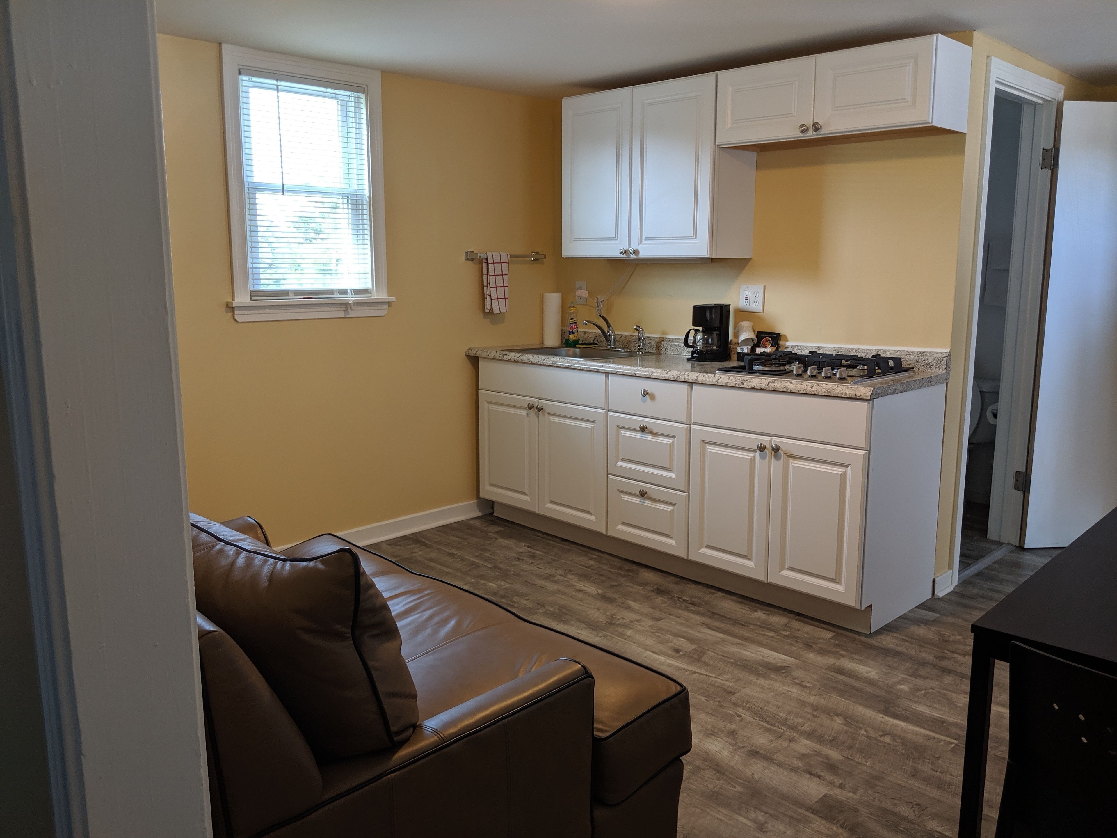 A compact kitchen with white cabinets, a countertop with a coffee maker, and a window with blinds.