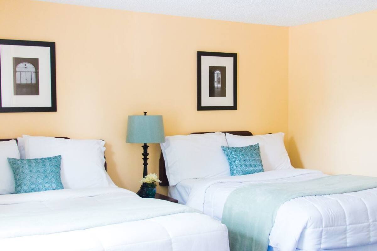 A hotel room with two beds, a nightstand with a lamp, and two framed pictures on the wall.