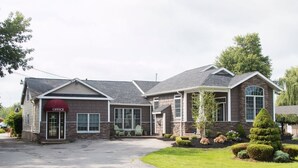 A two-story building with a stone facade, a red awning labeled "OFFICE," and a well-maintained lawn with trimmed bushes and a conifer. - Clarence Inn (Clarence)