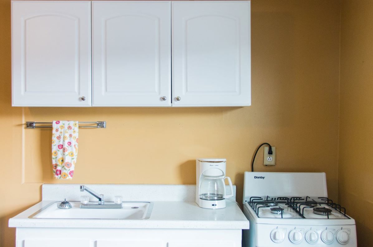 A kitchen with white cabinets, a coffee maker, a gas stove, and a sink.