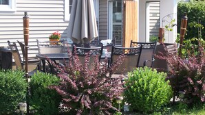 A patio with a table and chairs, a small covered area, and various plants. - Clarence Inn (Clarence)