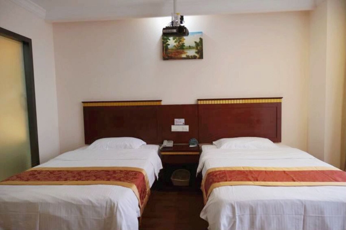 Una habitació d'hotel amb dos llits individuals, una tauleta de nit amb una làmpada i un quadre a la paret.