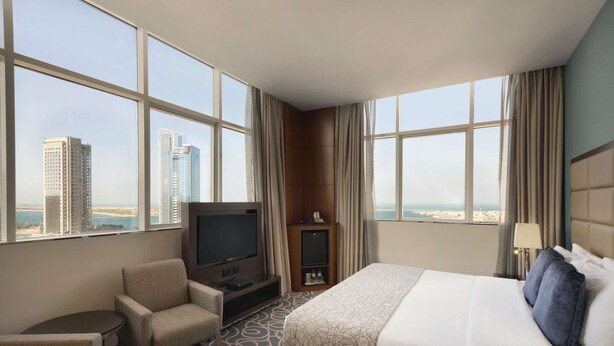 Une chambre d’hôtel avec un grand lit, une télévision, un coin salon et une vue sur de hauts immeubles.