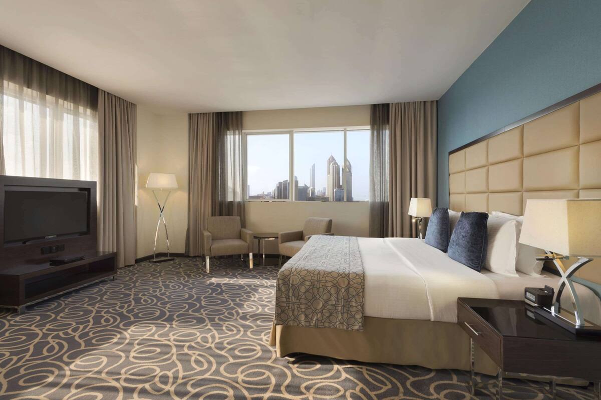 A hotel room with a large bed, a TV, a desk, and a view of the city skyline.