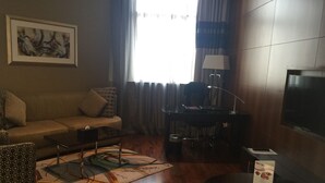 Un salon avec un canapé, une table basse et un téléviseur. On y trouve une lampe, une poubelle et un tapis.
