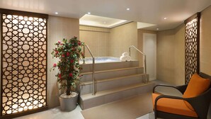 Un espace de détente avec un escalier menant à un bain à remous, une plante en pot et un coin salon comprenant une chaise et des coussins.