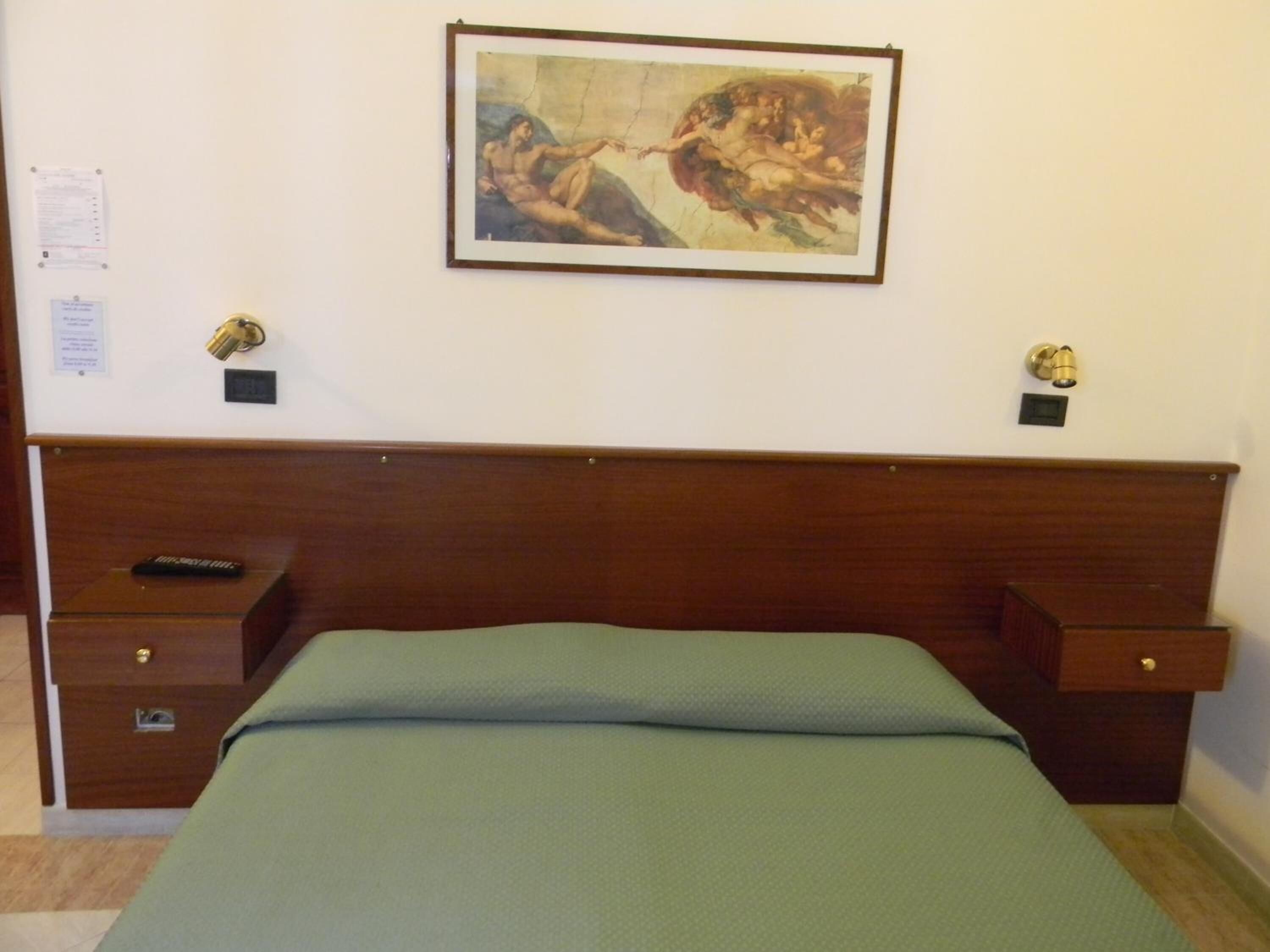 Habitación de hotel con cabecera de madera, cama con colcha verde, mesita de noche con control remoto y un cuadro enmarcado en la pared.