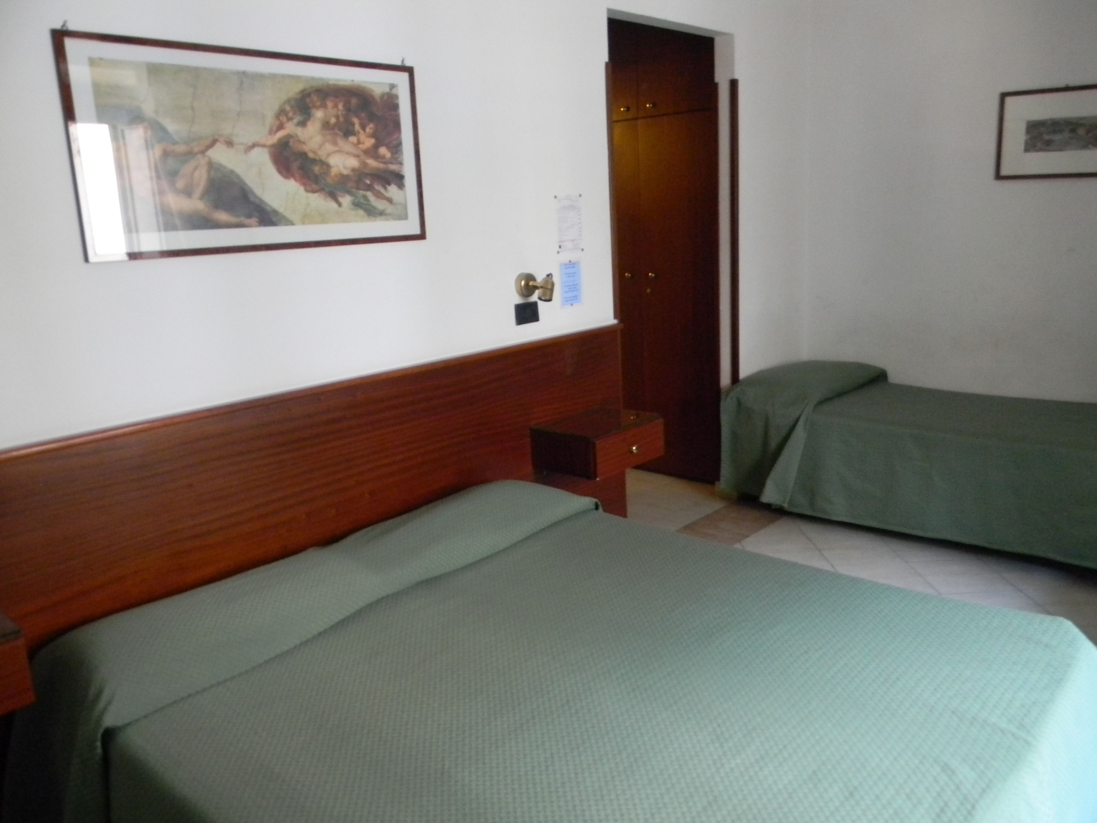 Une chambre avec deux lits, une tête de lit en bois, une porte et un tableau encadré au mur.