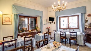 A dining area with tables set for meals, a chandelier, and a television on the wall. - Hotel Primavera (Rome)