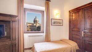 A hotel room with a bed, a window with a view of a dome, a wooden wardrobe, and a wall-mounted light fixture. - Hotel Primavera (Rome)