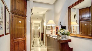 A hotel reception area with a marble floor, wooden reception desk, and a large mirror. - Hotel Primavera (Rome)