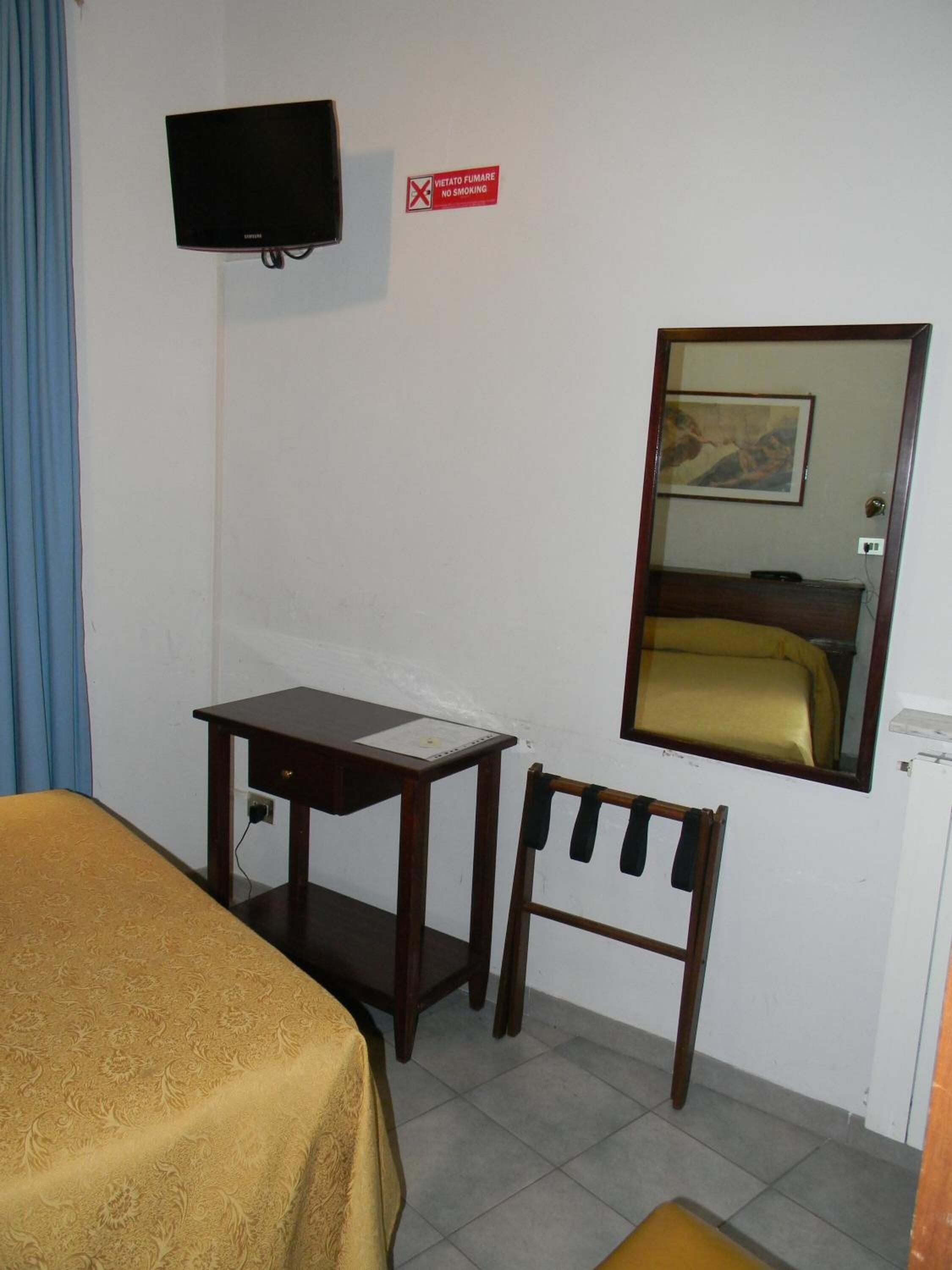 Una camera d'albergo con un letto, una scrivania, una sedia, un televisore e uno specchio.