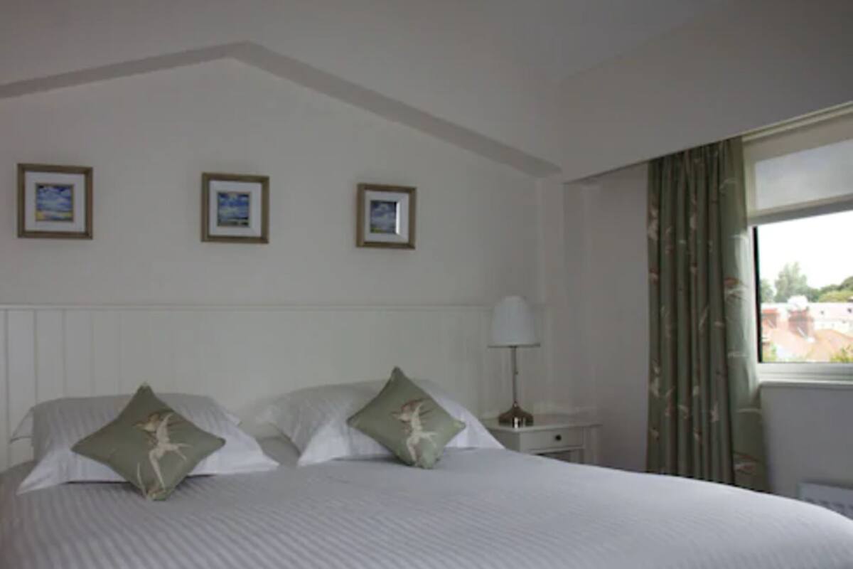 A hotel room with a large bed, two pillows, a nightstand with a lamp, and three framed pictures on the wall.