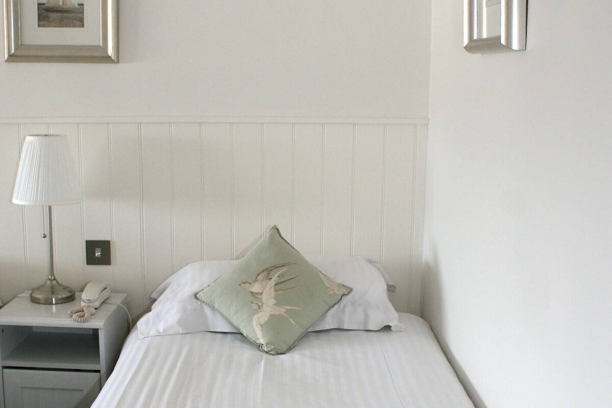 A neatly made bed with a pillow, a bedside lamp, and a framed picture on the wall.