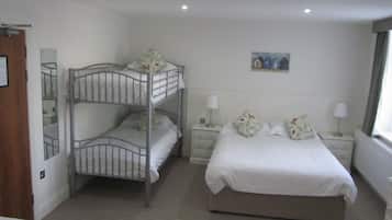 A hotel room with bunk beds, a single bed, a nightstand with lamps, a painting on the wall, and a window with curtains.