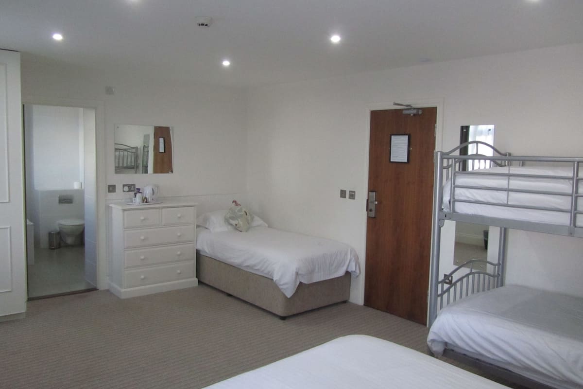A bedroom with a bunk bed, a single bed, a dresser, a mirror, and a door.