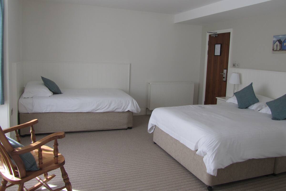 A hotel room with two single beds, a wooden rocking chair, a radiator, and a door with a sign.