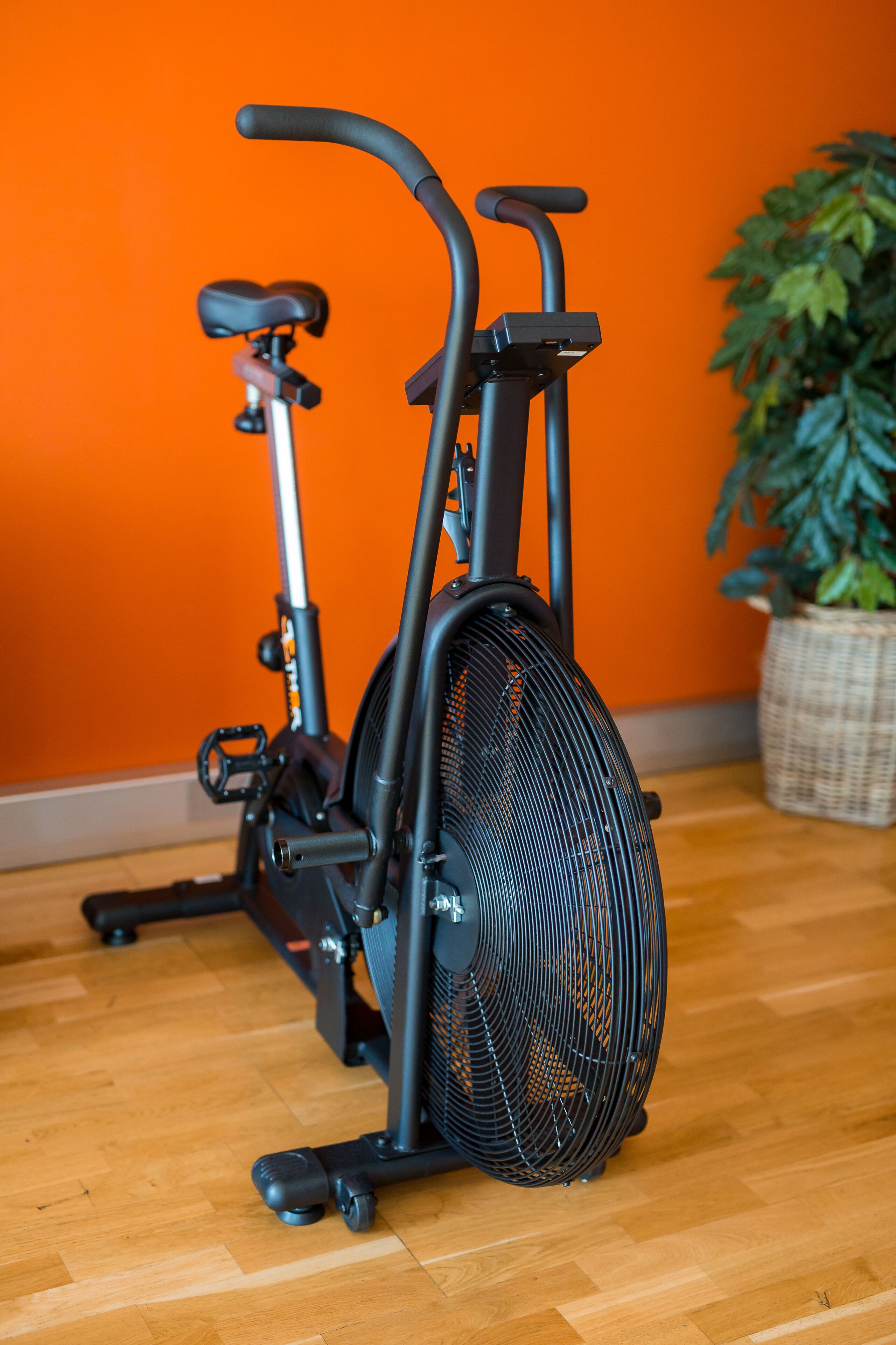 Una bicicleta estática en una habitación con suelo de madera y pared naranja.