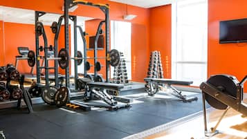 Un gimnasio con equipo de levantamiento de pesas, una banca y una cinta de correr.