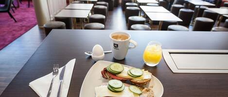 Un desayuno con un plato de sándwiches, una taza de café y un vaso de jugo de naranja sobre una mesa.