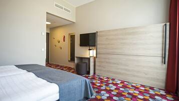 Habitación de hotel con dos camas, televisión, armario y alfombra estampada.