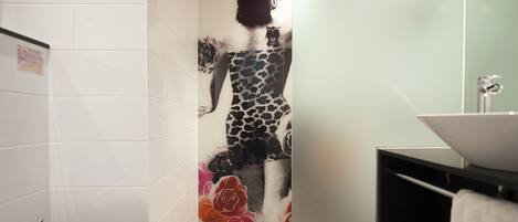 A bathroom with a tiled wall, a white sink, and a shower area.
