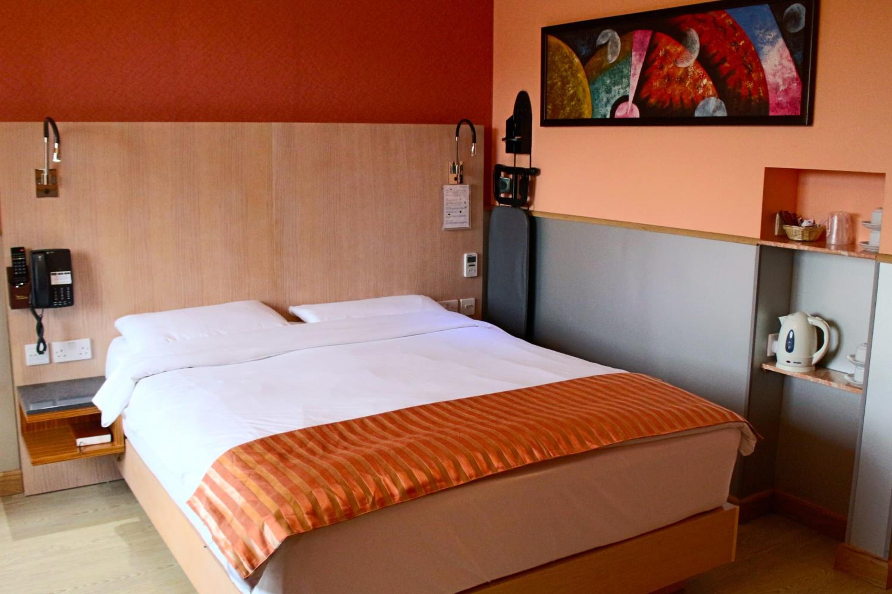 Een hotelkamer met een bed, een telefoon, een waterkoker en een plank met toiletartikelen.