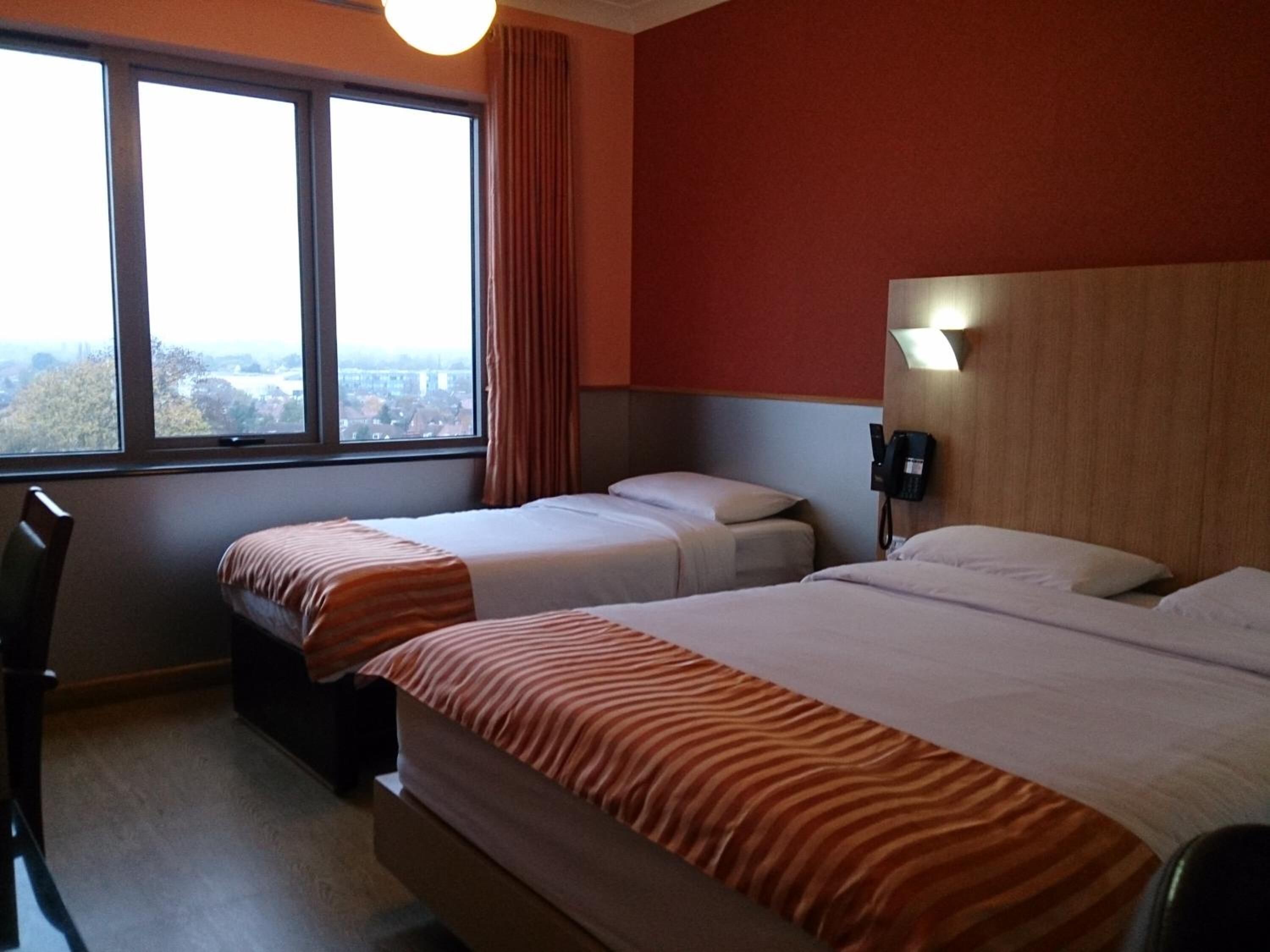 A hotel room with two beds, a view of the city through large windows, and a telephone on the wall.