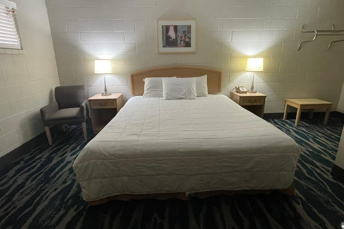 A hotel room with a large bed, two bedside tables with lamps, a chair, a small table, and a picture on the wall.