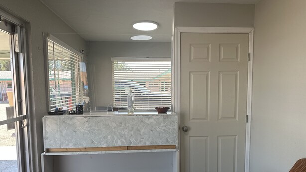 A kitchen with a marble countertop, a sink, and a window with blinds.