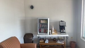A small room with a striped couch, a table with a refrigerator, a coffee maker, and a trash can.