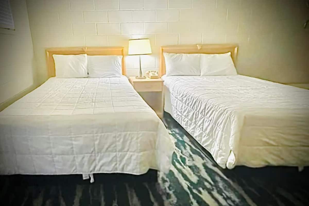 A hotel room with two single beds, each with a wooden headboard, a bedside table with a lamp, and a telephone.