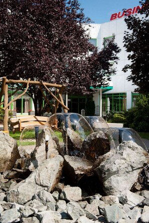 A water feature with rocks and a wooden structure in a landscaped area with a building in the background.