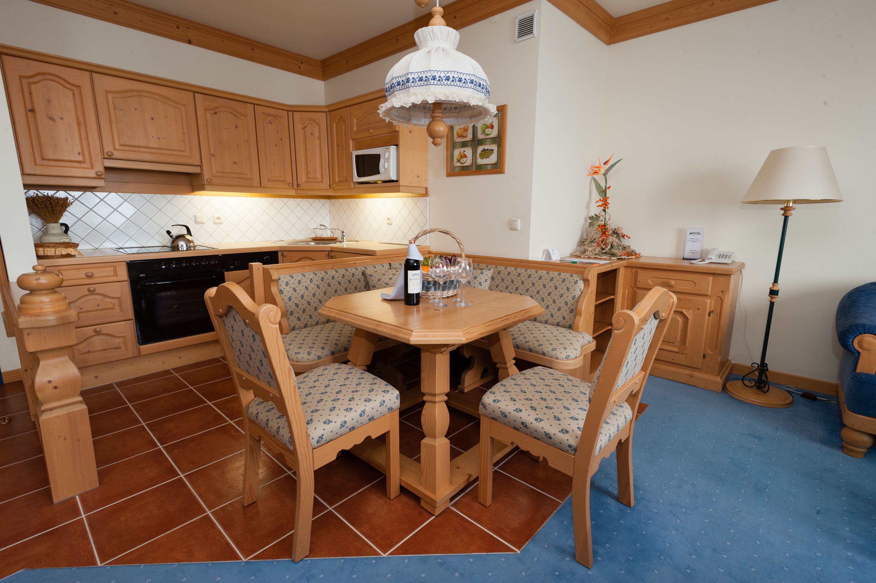 A kitchen with wooden cabinets, a microwave, a dining table with four chairs, and a floor lamp.