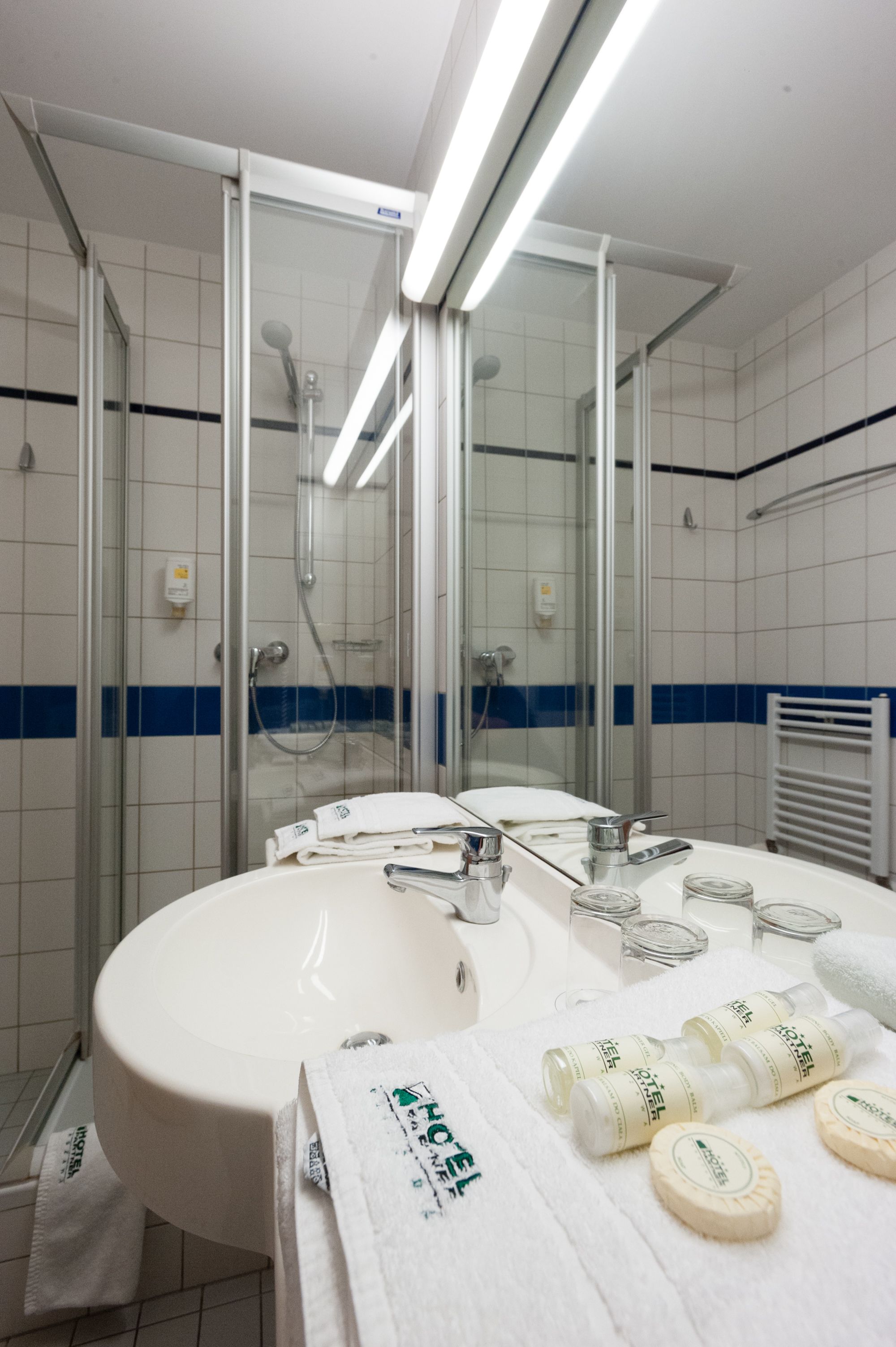 A modern bathroom with a glass-enclosed shower, a white sink with a mirror, and toiletries on the counter.