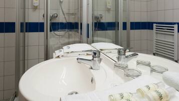 A modern bathroom with a glass-enclosed shower, a white sink with a mirror, and toiletries on the counter.