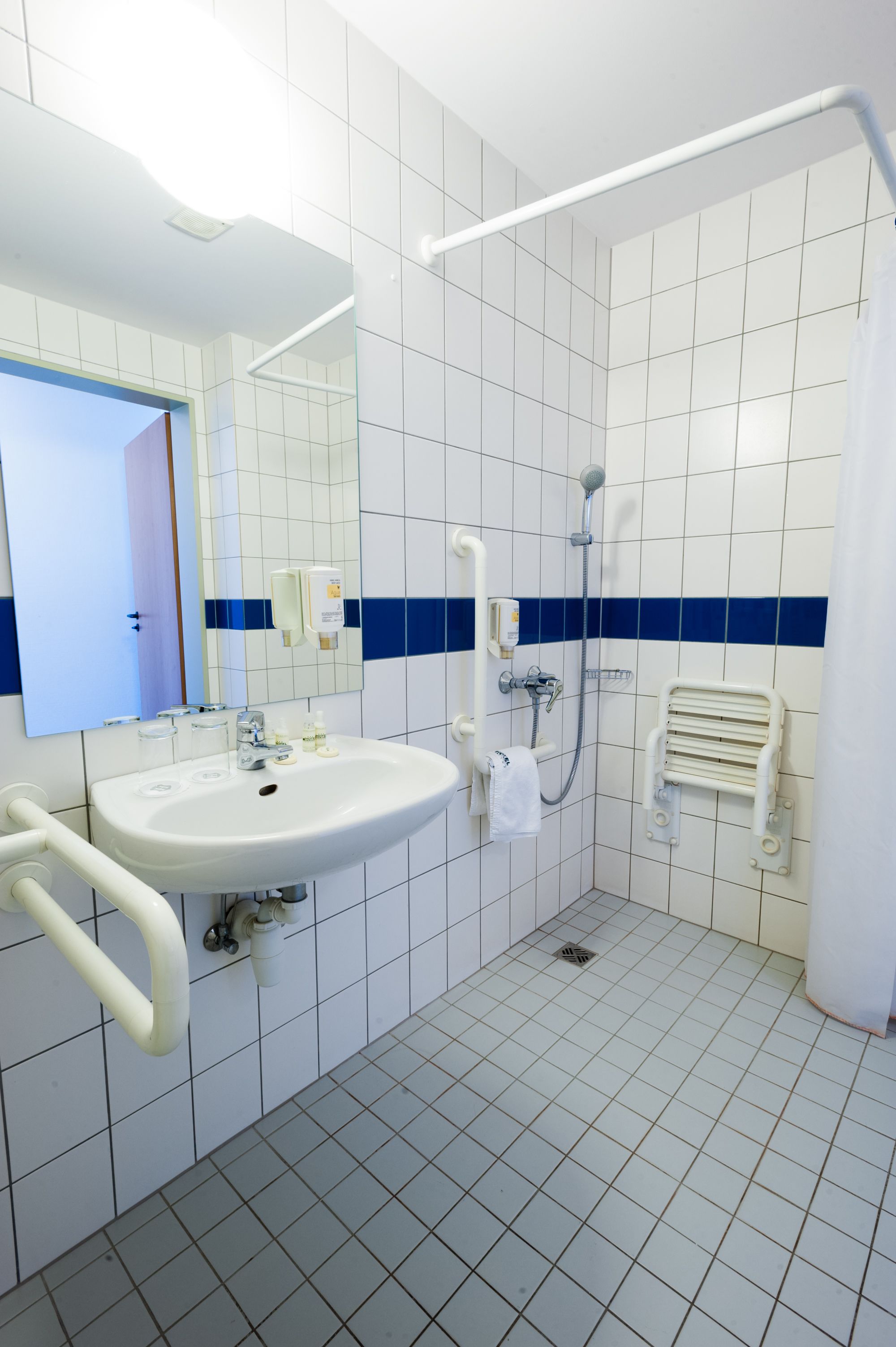 A bathroom with a white sink, mirror, and a shower with a handheld showerhead.