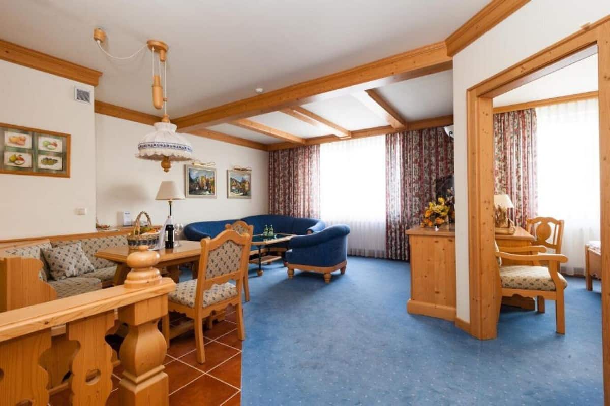 Una habitación con techo de madera, alfombra azul, sofá, mesa de comedor con sillas y candelabro.