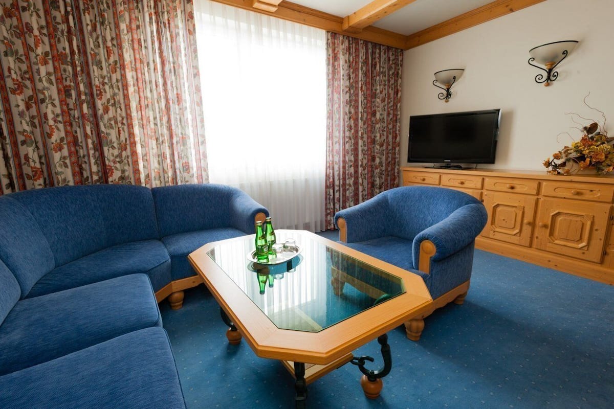 Una sala de estar con sofás azules, una mesa de centro de vidrio, un televisor y armarios de madera.